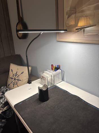 Desk with angled lamp, record organizer with pens and cards, a pillow with compass design, and a mandolin connected the wall
