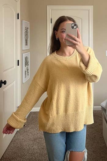 Person taking a selfie successful a casual oversized sweater and ripped jeans successful a minimal chamber setting