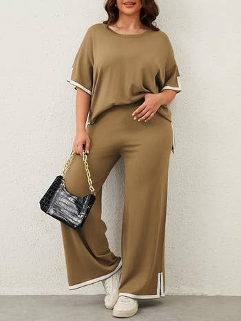 model wearing a loose-fitting pullover and wide-leg pants, holding a quilted handbag, wearing achromatic sneakers