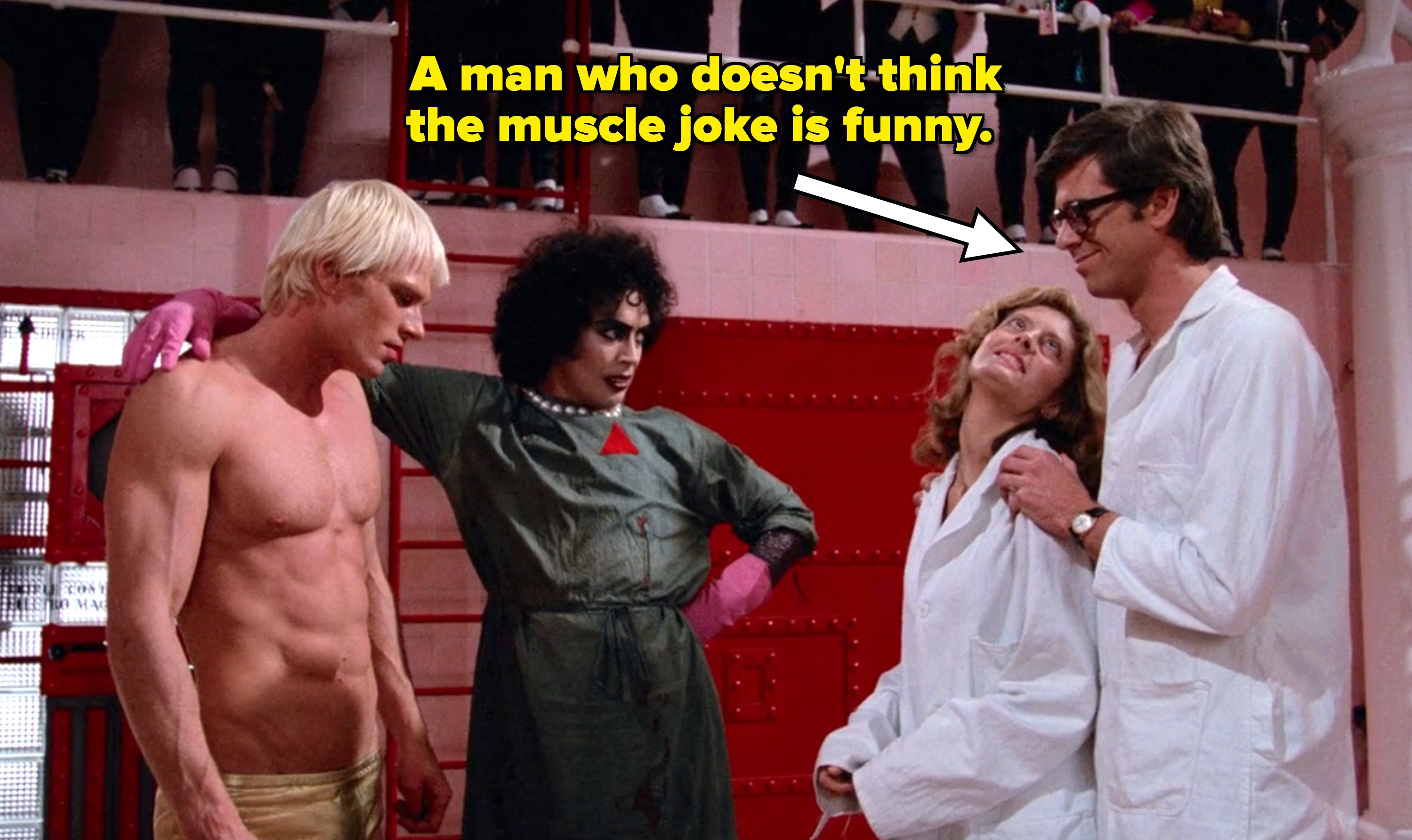 a shirtless man, a figure in a dramatic outfit, and two in lab coats, share a moment onstage