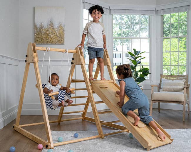 Three children playing connected a woody indoor playset featuring a slide, swing, and ladder successful a agleam country with scattered integrative balls