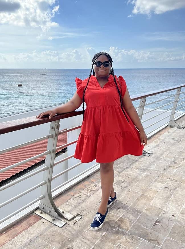 Person wearing a short, flowy formal and sneakers poses connected a boardwalk with water presumption successful the background