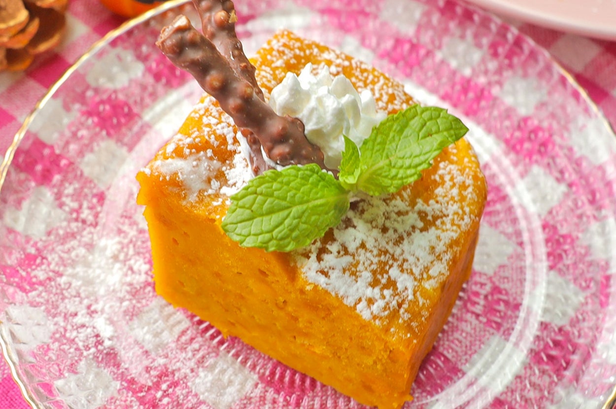 デザートのパンプキンケーキにホイップクリームとミントがトッピングされています。背景にかぼちゃの飾りがあります。