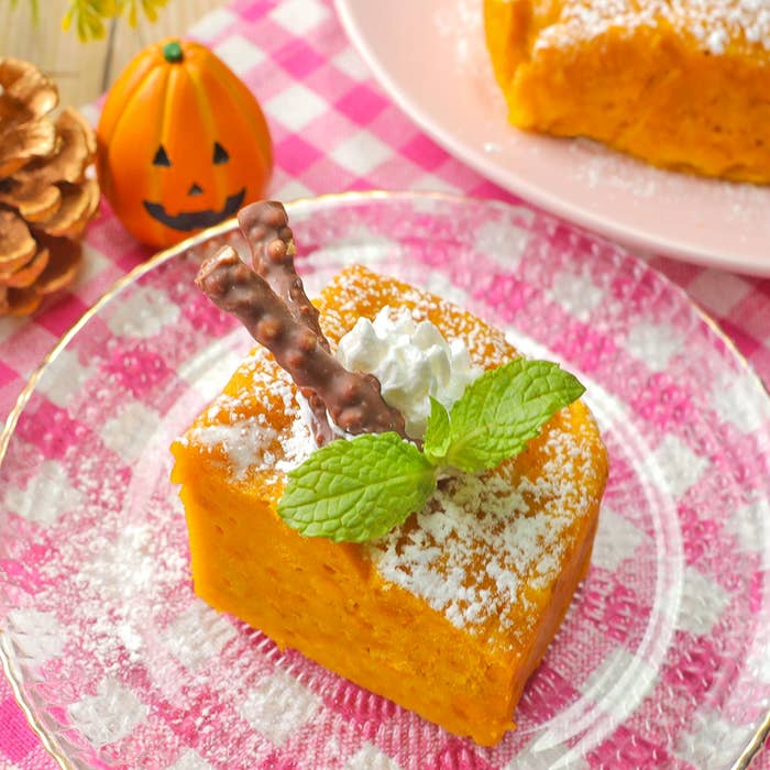 デザートのパンプキンケーキにホイップクリームとミントがトッピングされています。背景にかぼちゃの飾りがあります。