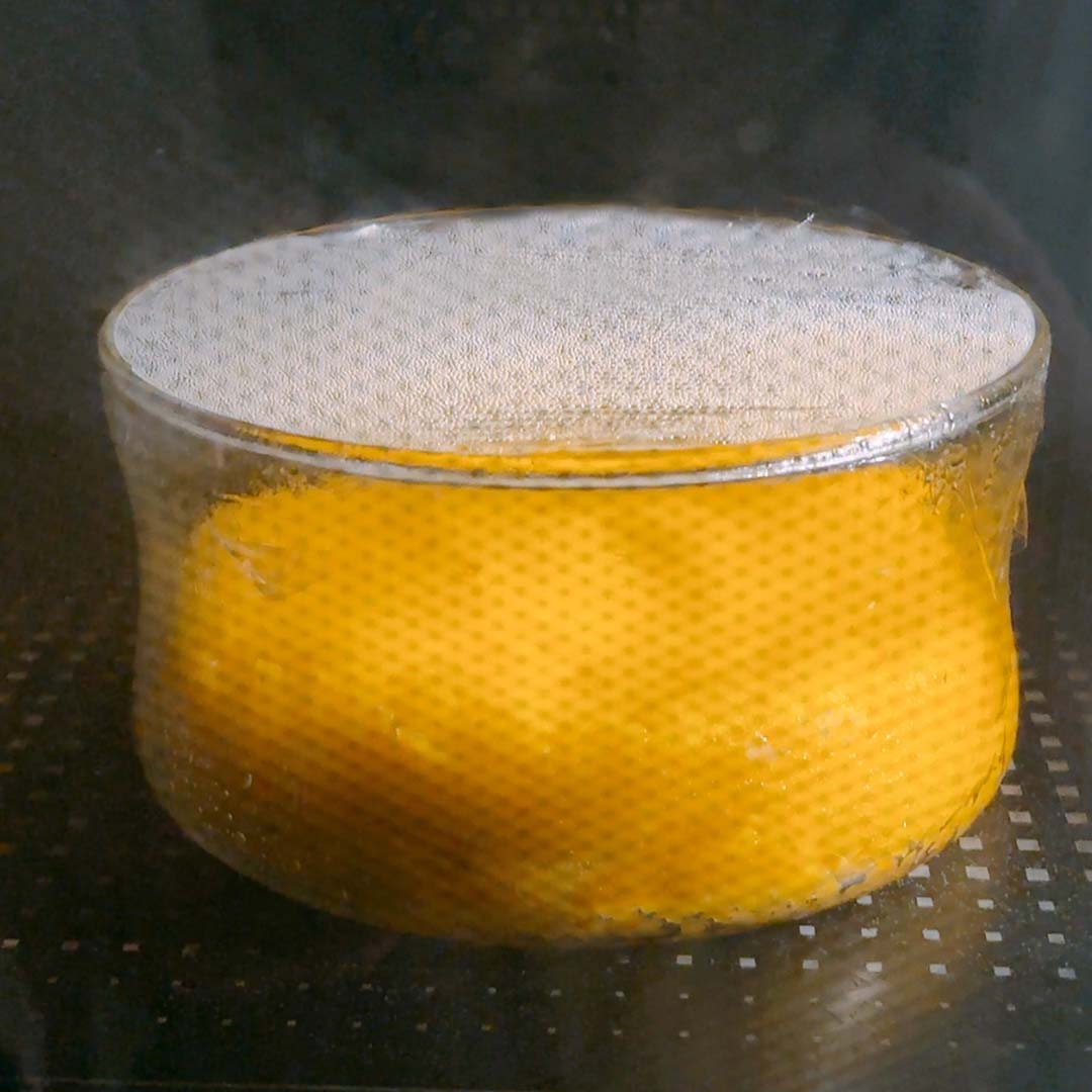 電子レンジ内のガラス容器に入ったラップがけの黄色いケーキが蒸気を出しながら加熱されている。