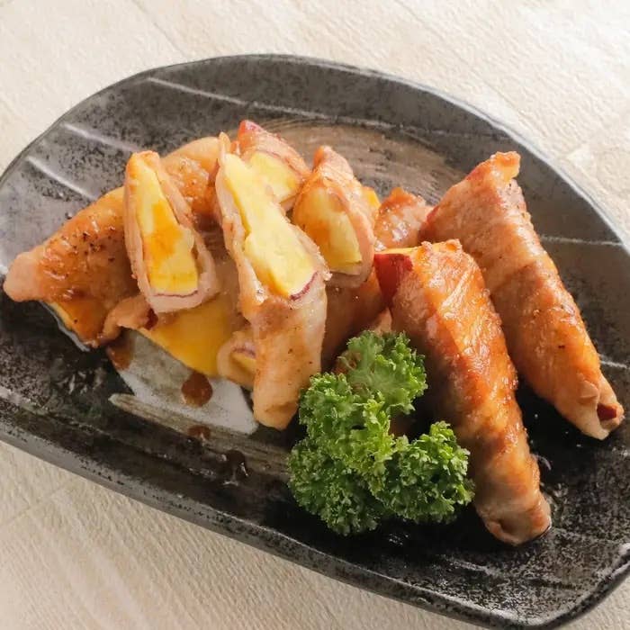 肉で巻かれたチーズ入りの卵料理が黒い皿に盛り付けられており、横にパセリが添えられています。