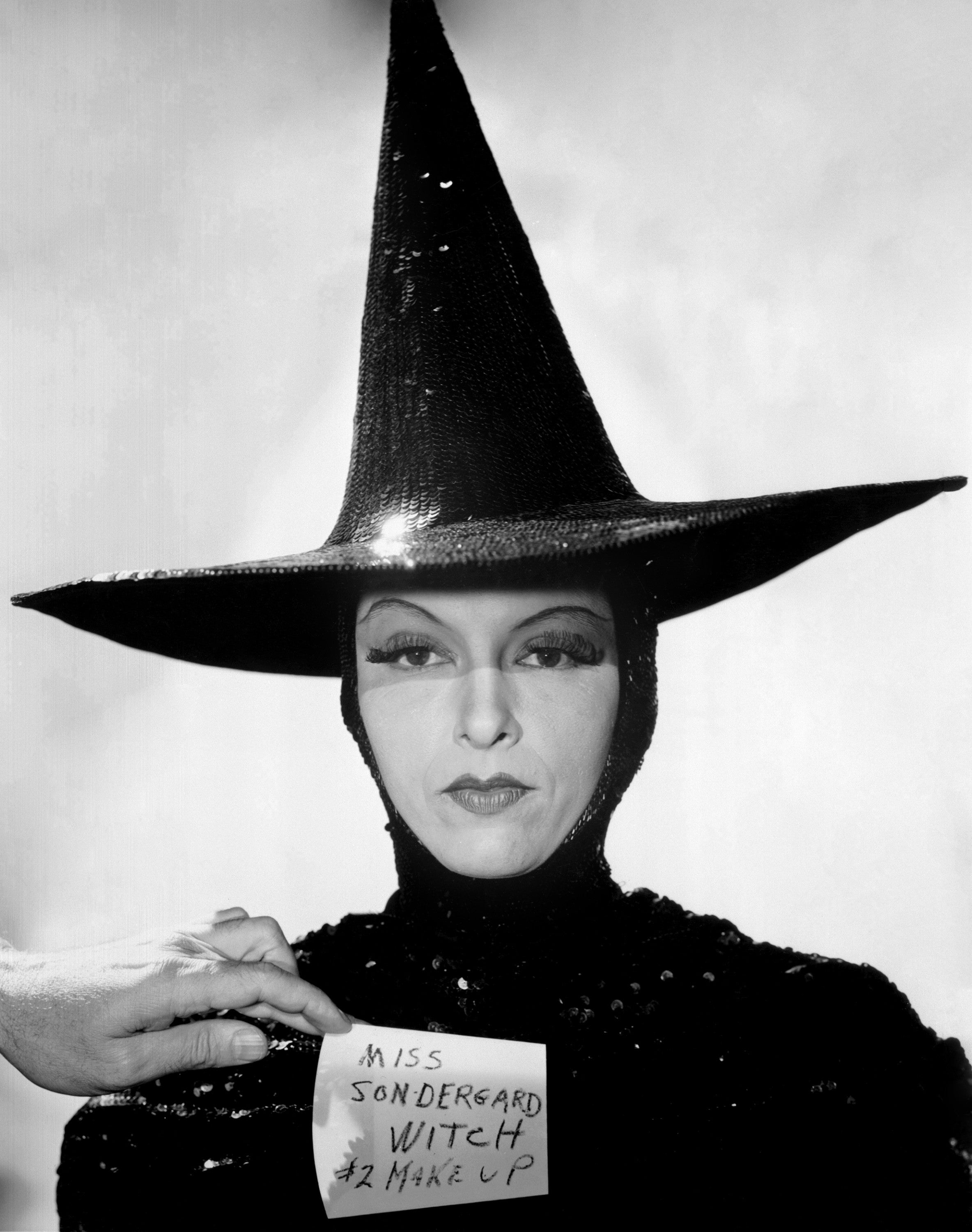 Person posing successful a sequined outfit with a gangly pointed hat, holding a enactment speechmaking "Miss Sondergard Witch #2 Makeup."