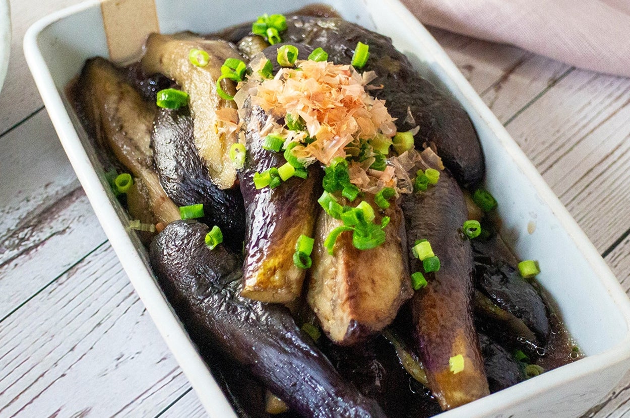 長方形の白い皿に焼きナスが盛られ、細かく切ったネギと削り節がトッピングされています。
