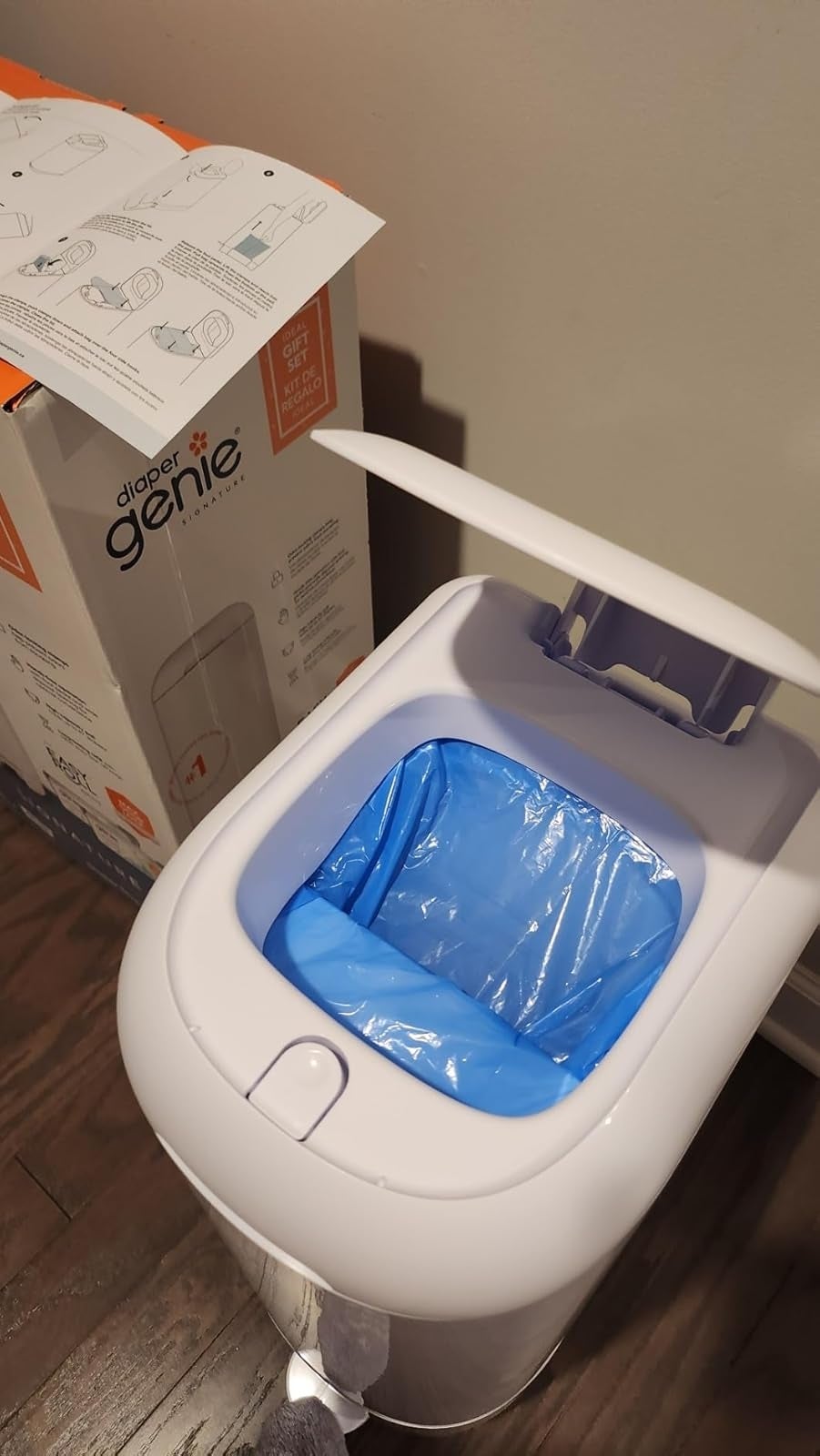 Open diaper pail with a bluish  liner inside, instructions above. Box labeled 