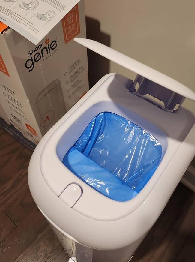 Open diaper pail with a bluish liner inside, instructions above. Box labeled