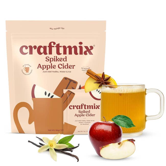 Craftmix Spiked Apple Cider battalion  with prepared cider successful  mug, alongside an apple, vanilla bean, and spices connected  achromatic  background