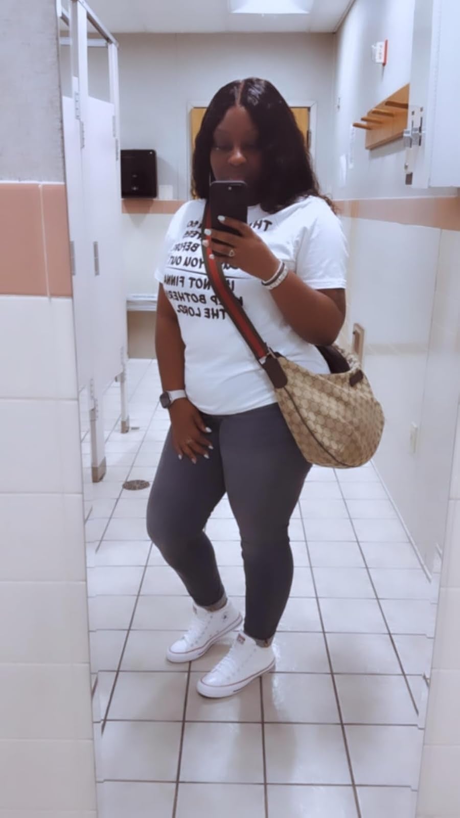 Person taking a reflector  selfie successful  a restroom, wearing a printed t-shirt, jeans, achromatic  sneakers