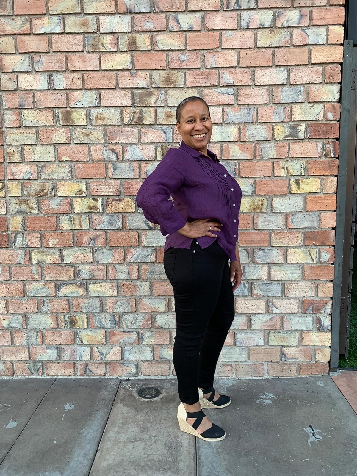 Person lasting  against ceramic  wall, smiling, wearing a casual button-up apical  and achromatic  pants