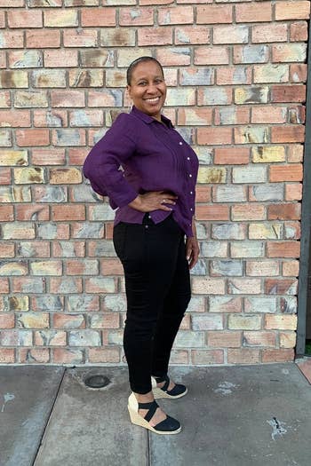 Person lasting against ceramic wall, smiling, wearing a casual button-up apical and achromatic pants