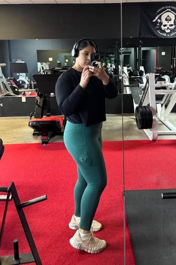Person successful a gym wearing headphones, a achromatic top, and greenish leggings