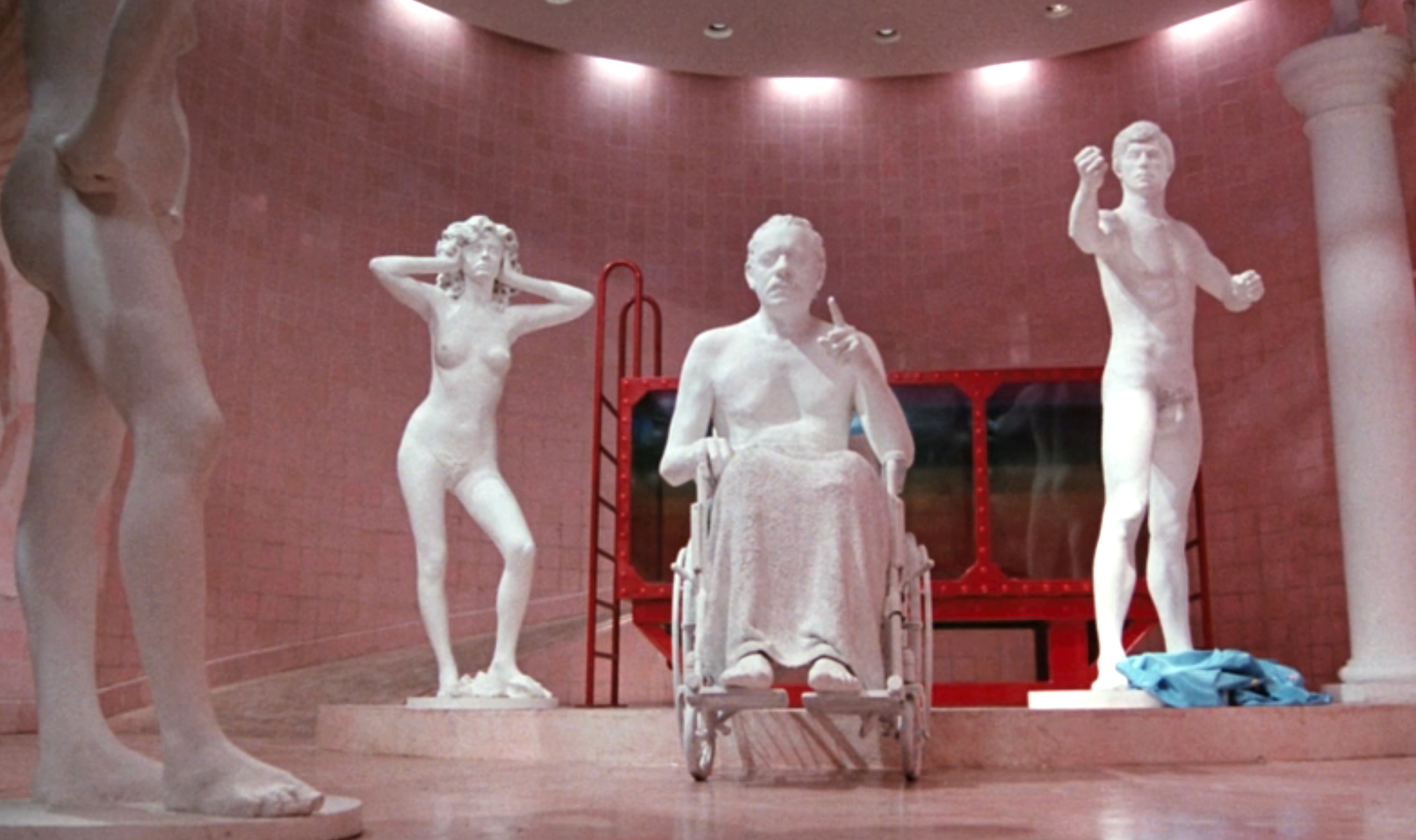 Three marble statues depicted in a museum setting, including one in a wheelchair