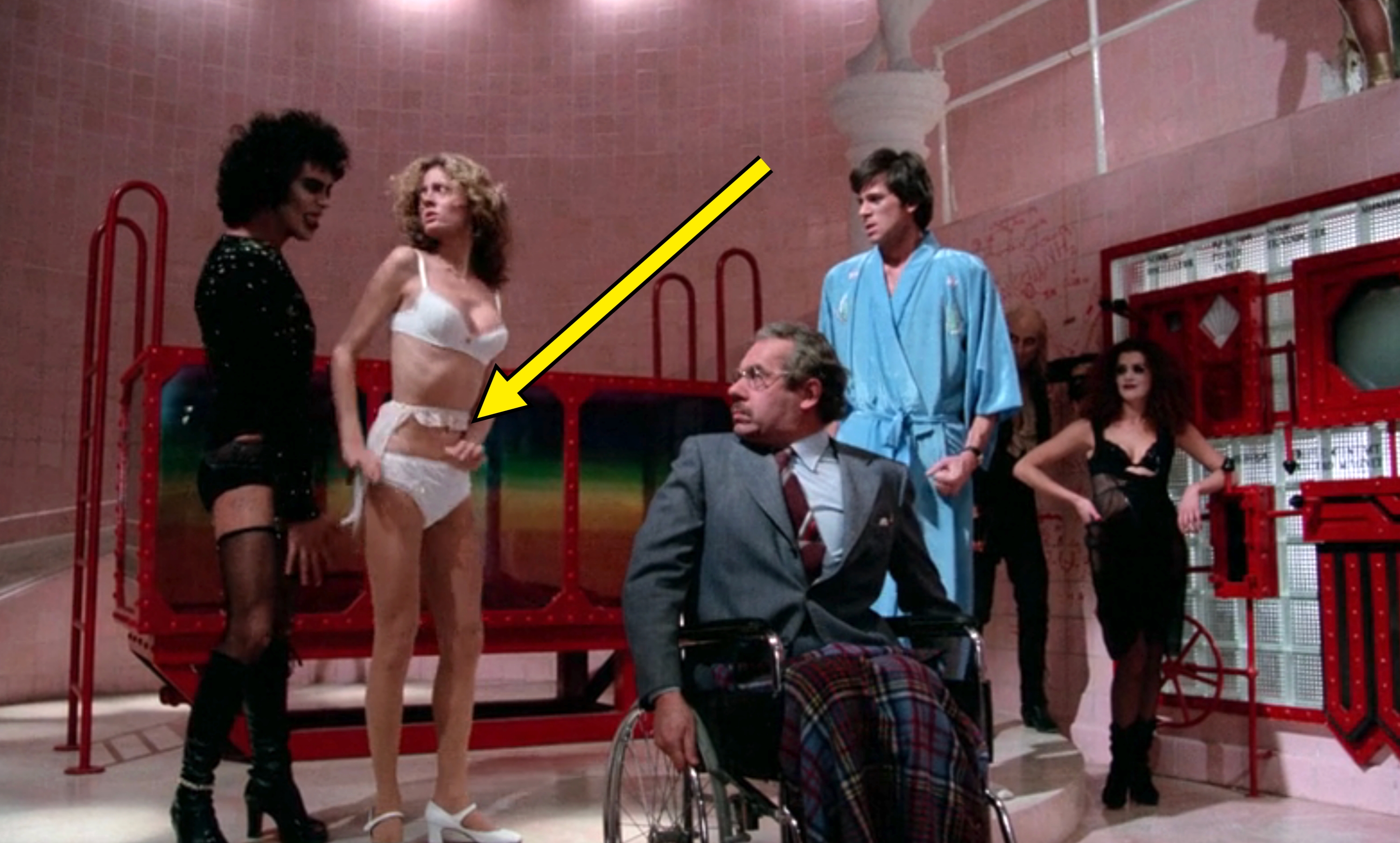 Scene from a theatrical performance with characters in eclectic costumes, including a man in a wheelchair, interacting dramatically