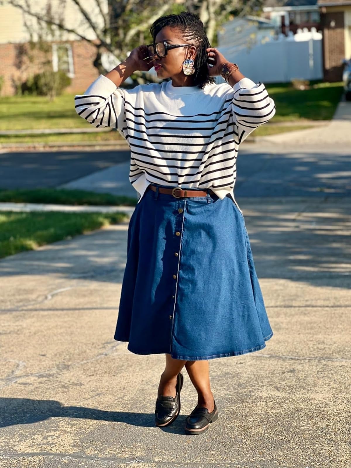  striped sweater, buttoned denim skirt, loafers, and ample  earrings, lasting  with hands adjusting glasses