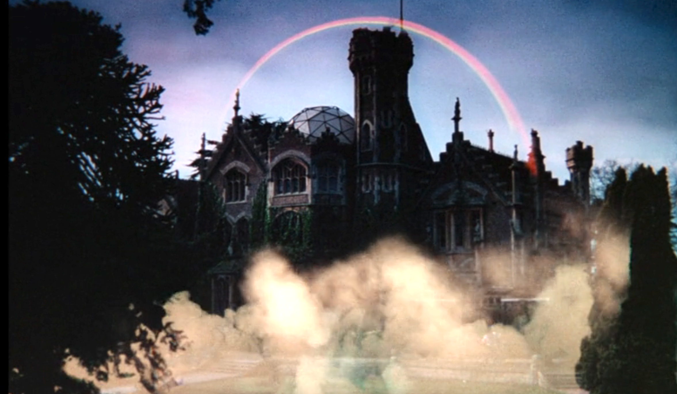 Gothic-style mansion with a domed roof, surrounded by mist and framed by a rainbow in the sky