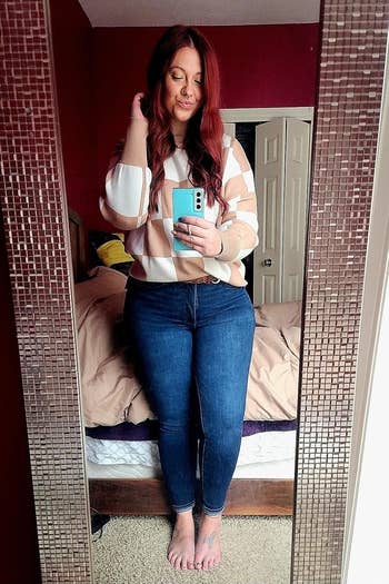 Person takes a reflector selfie wearing a checkered sweater and jeans