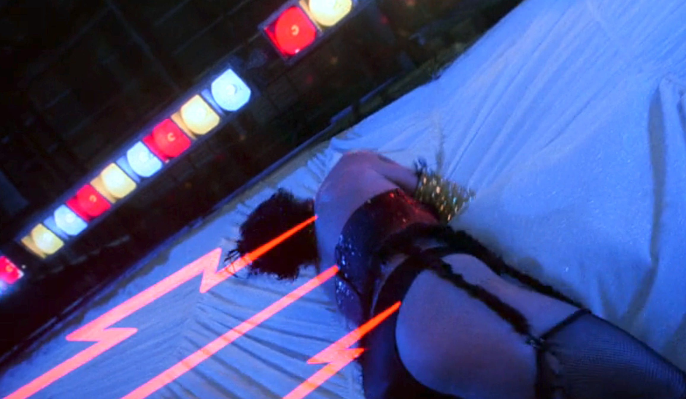 A performer in a revealing outfit is seen lying on a stage with bright lights and dynamic neon red lines in the background