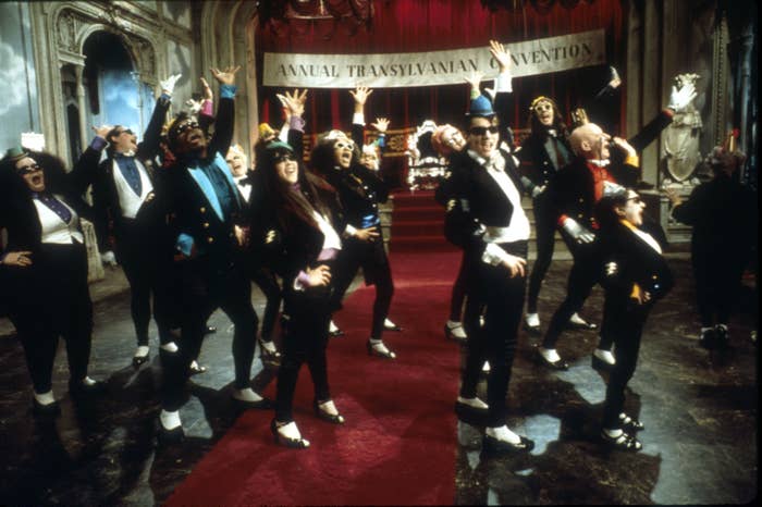 Group of people in costumes performing at the Annual Transylvanian Convention, striking exaggerated poses in a theatrical scene