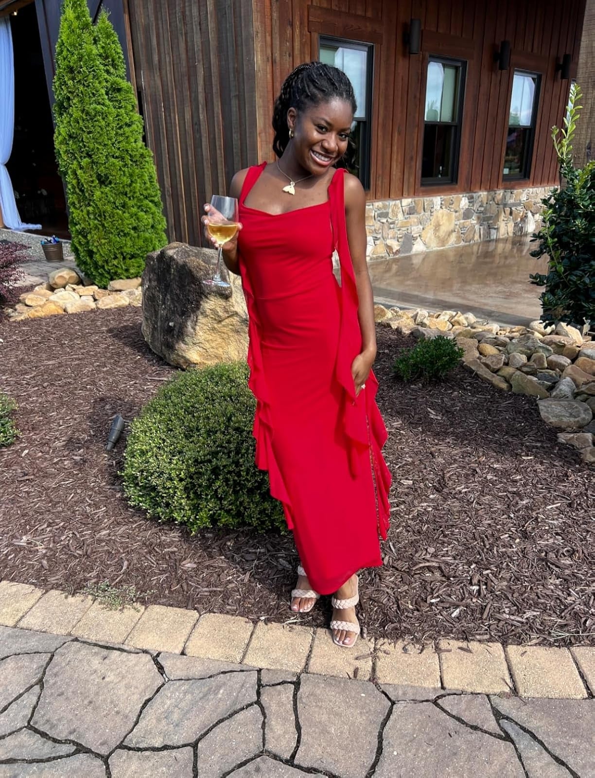 Person posing outdoors successful  a sleeveless, tiered formal  holding a drink, smiling