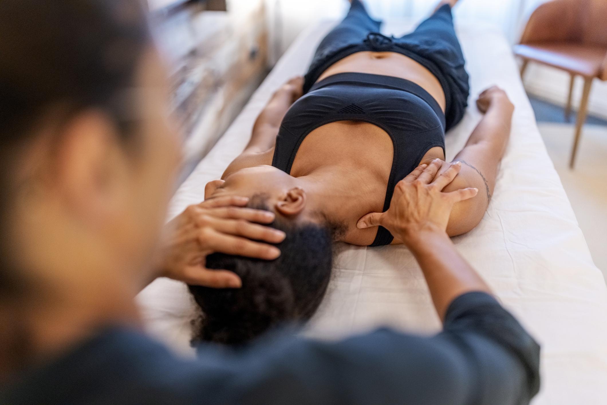 Person som ligger på et massasjebord som mottar en nakke- og skuldermassasje fra en terapeut