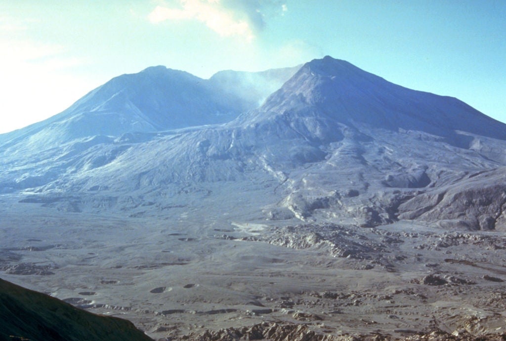 Mount St. Helens with a rugged landscape; smoke rises from the crater, indicating volcanic activity