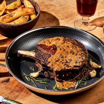 Cooked steak with peppercorn condiment connected a pan, garnished with rosemary and garlic, served with a vessel of murphy wedges and a solid of reddish wine