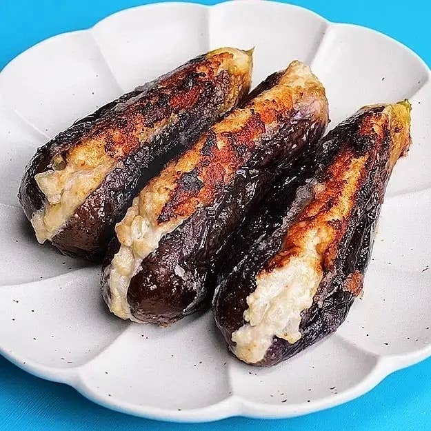 焼きナスが皿に3本並んでいる。表面は香ばしく焼かれ、皮がぱりっとした質感になっている。