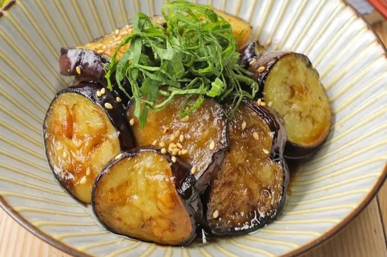 白い器に盛られたナスの料理。上に細く刻んだ薬味がのっており、ごまが散らされています。テーブルに箸が置かれています。