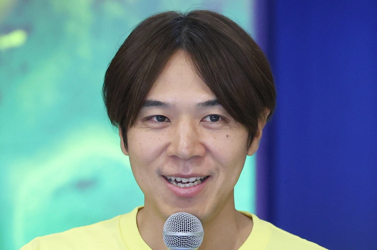 申し訳ありませんが、この画像に映っている方が誰かはわかりません。マイクを持った方が、カジュアルなTシャツを着て話しています。