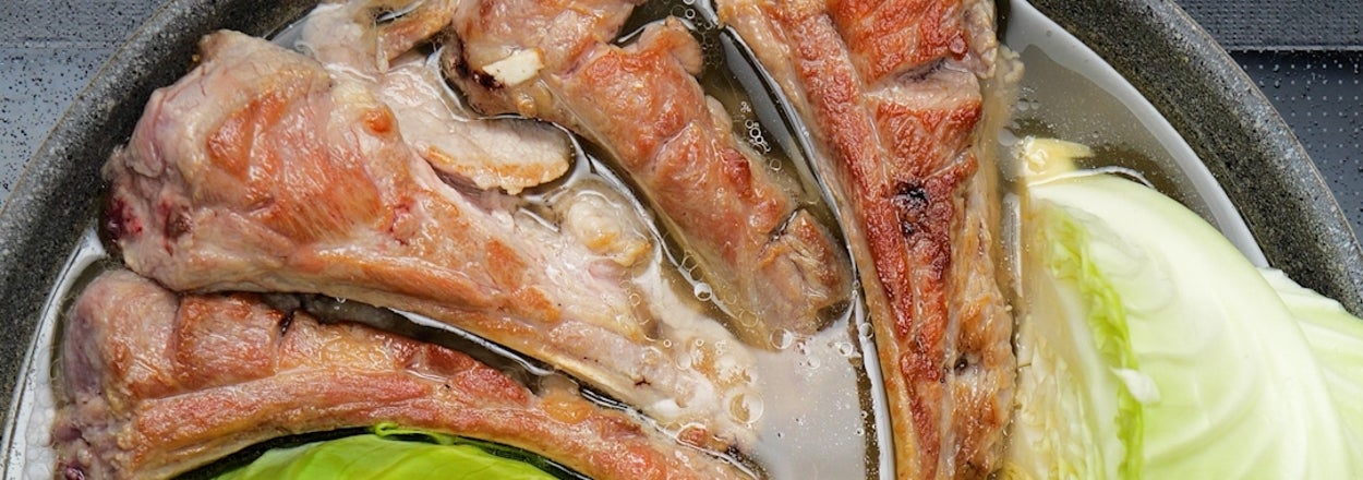 鍋で骨付き肉とキャベツが調理されている様子。