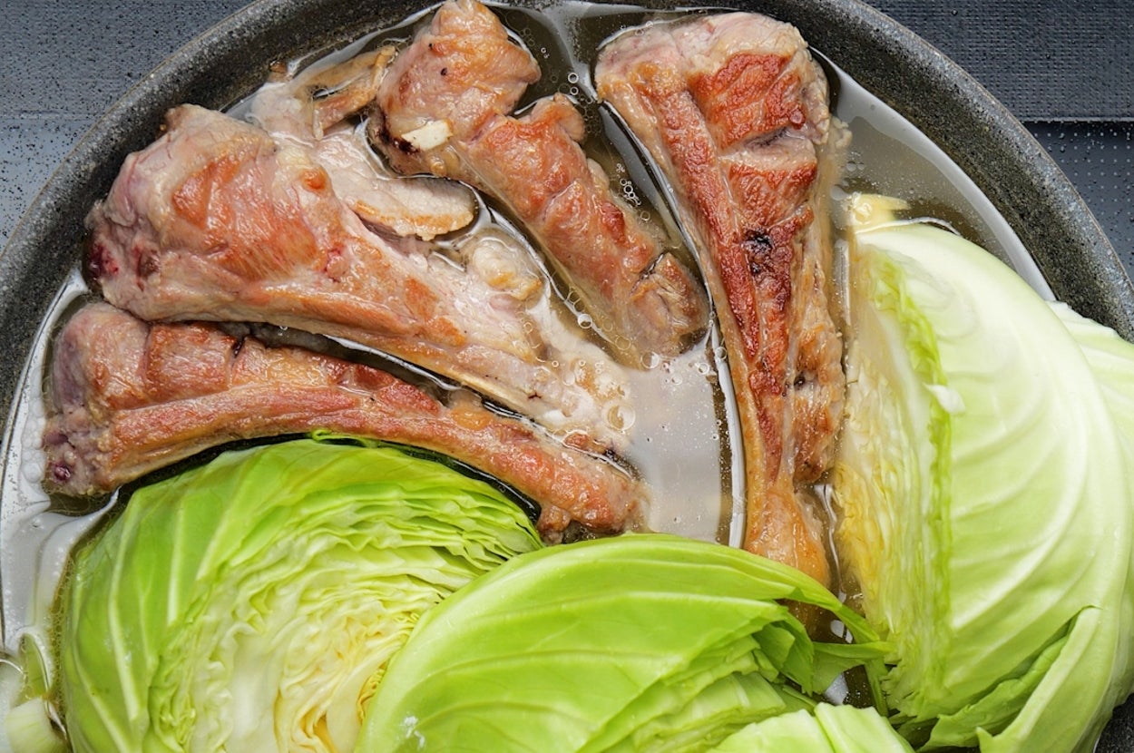 鍋で骨付き肉とキャベツが調理されている様子。