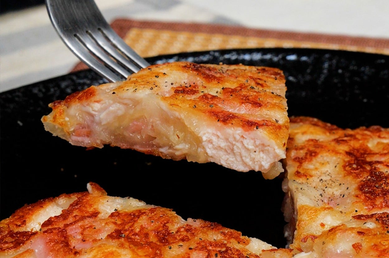 フライパンでジュージュー焼かれたピザ風の料理がフォークで持ち上げられている。サクサクした食感を想像させる。