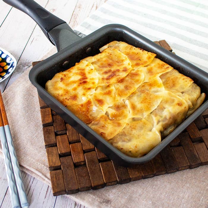 焼きたての餃子が四角いフライパンに並べられている。左には箸が添えられている。