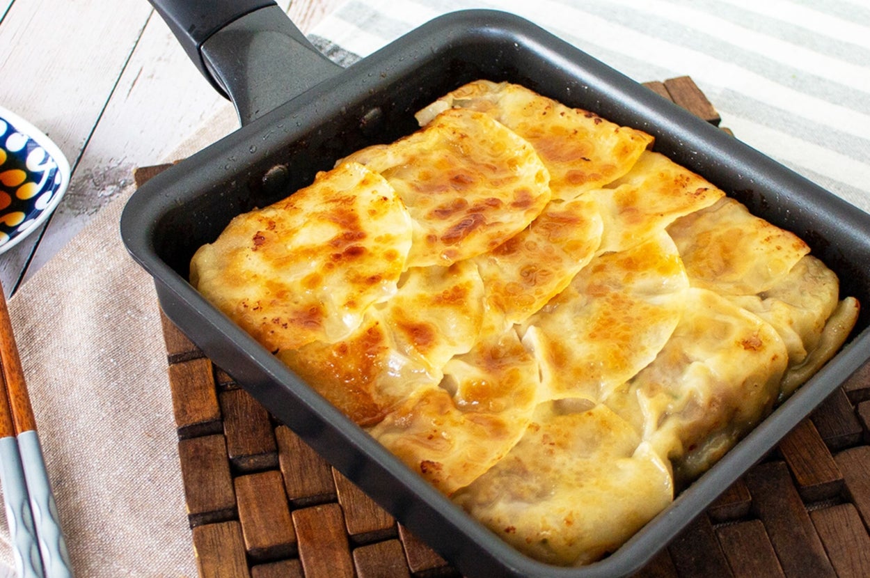 四角いフライパンで焼かれた餃子。焼き目が付いて美味しそうに見える。隣に箸が置かれている。