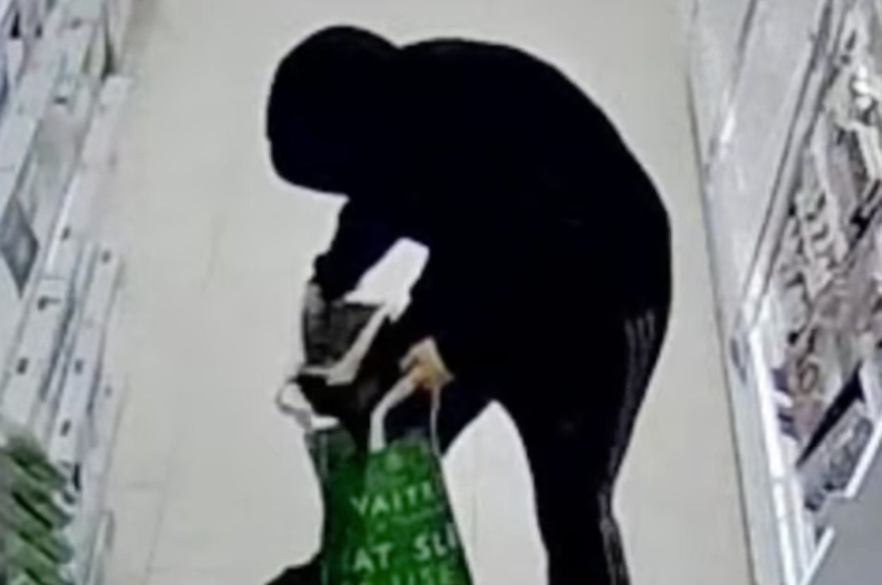 店内でフードを被り手提げ袋に商品を入れる人物。
