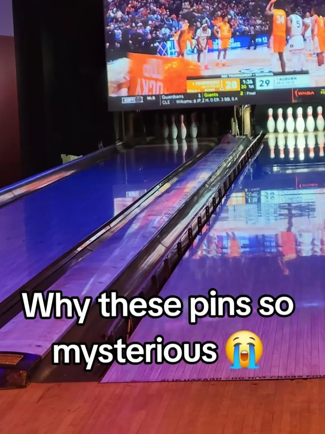Bowling alley with pins and a ball return. A game appears on a large screen. Text reads: &quot;Why these pins so mysterious&quot; with a crying emoji