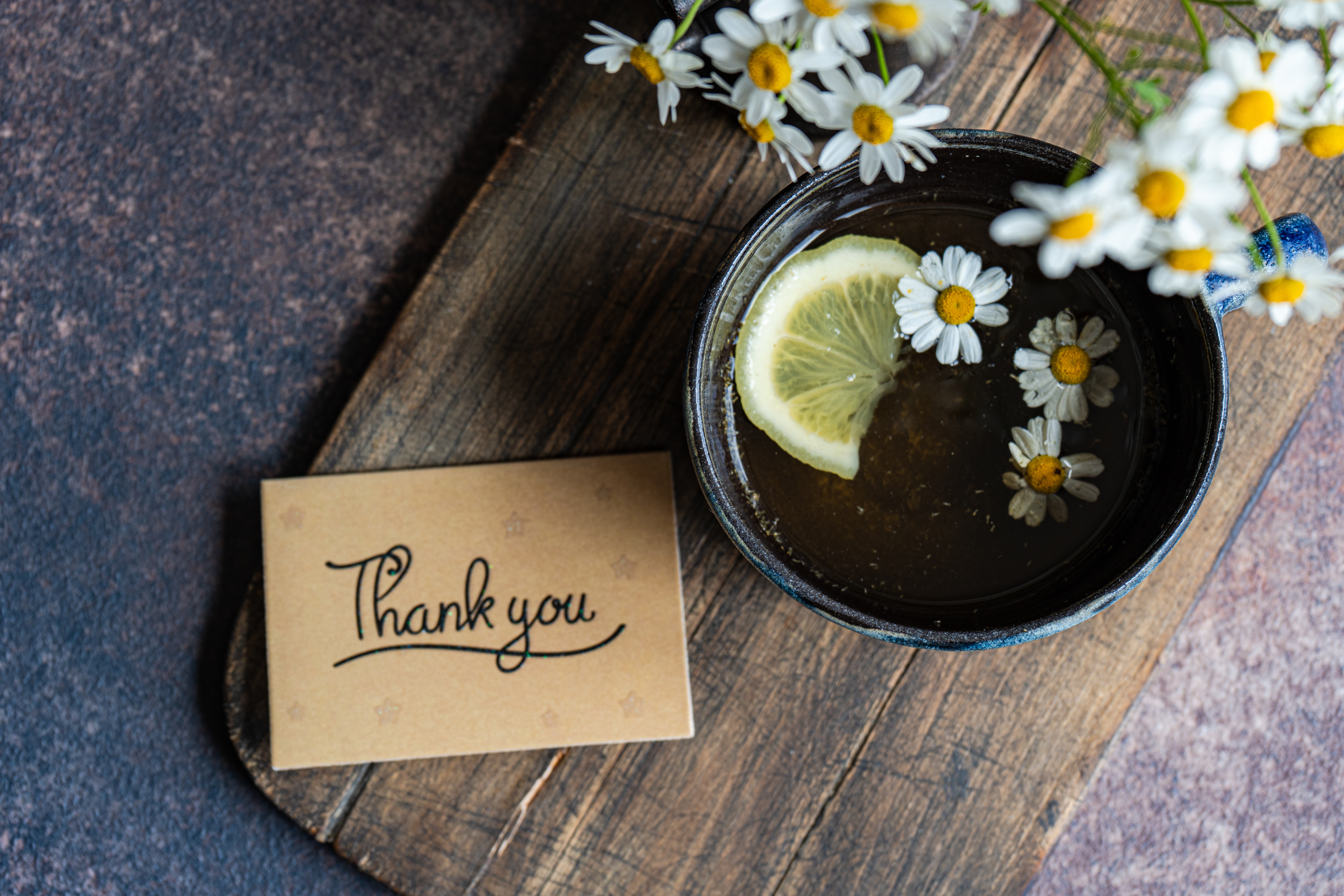 En kopp te med sitron- og kamilleblomster ved siden av et kort som sier & quot; takk & quot; på et trebrett
