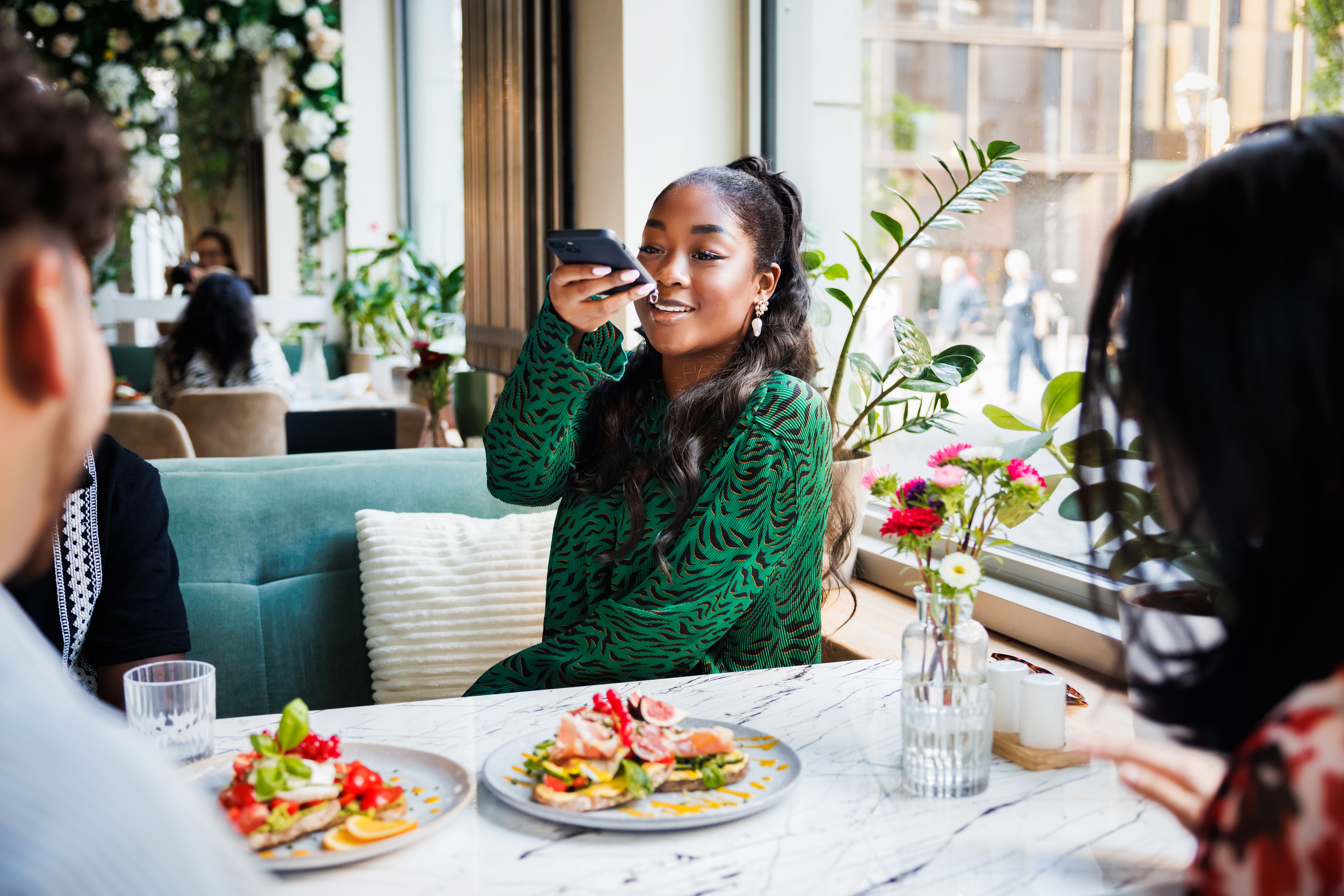 Person i en mønstret skjorte tar et smarttelefonbilde av mat ved et restaurantbord med venner