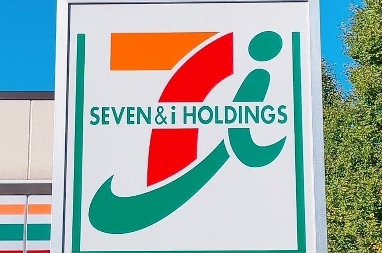 「SEVEN & i HOLDINGS」の看板が映る画像。店舗の一部と木々が背景に見える。