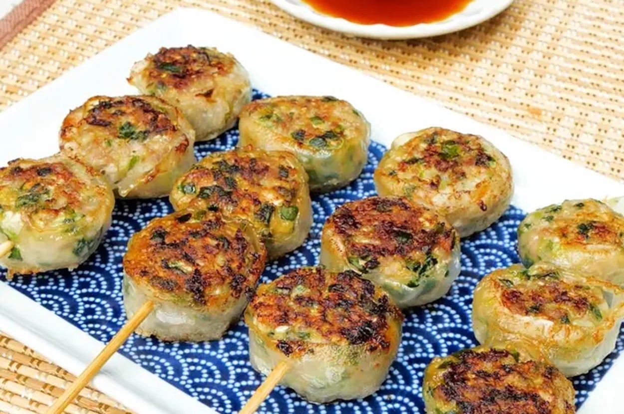 焼き色の付いた串付き焼き餃子が皿に並べられている。ソースが小皿に入っている。