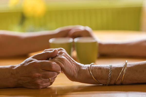 Two pairs of hands affectionately holding each other across a table with two cups in the background, suggesting companionship and intimacy