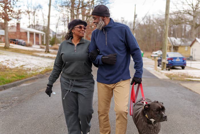 An older couple walks arm in arm down a suburban street with their dog, sharing a loving moment outdoors