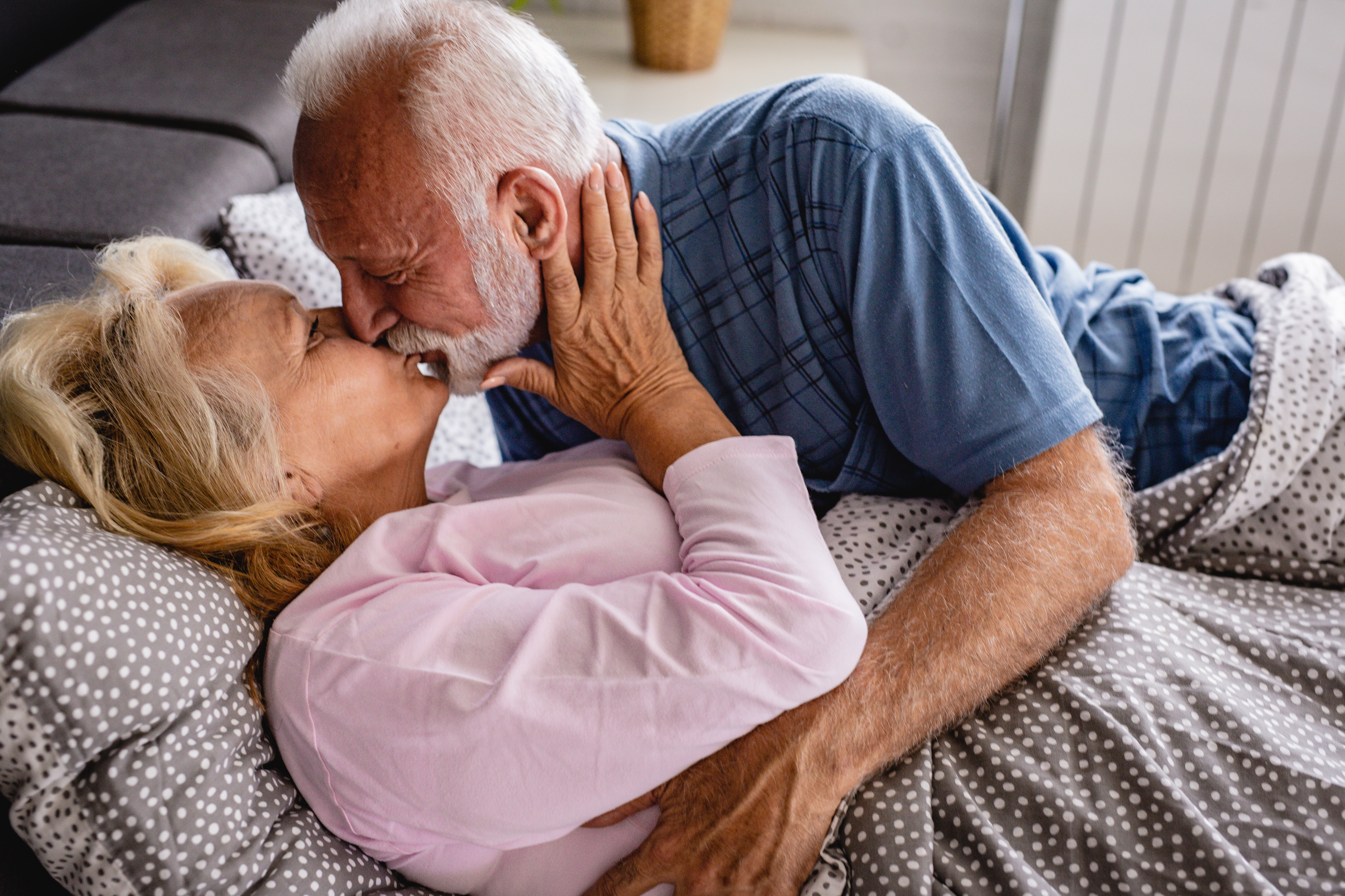 Older couple gently kissing while lying in bed, embracing each other affectionately
