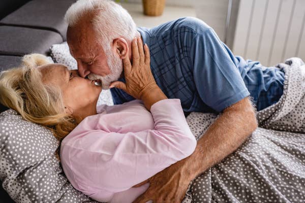 Older couple gently kissing while lying in bed, embracing each other affectionately