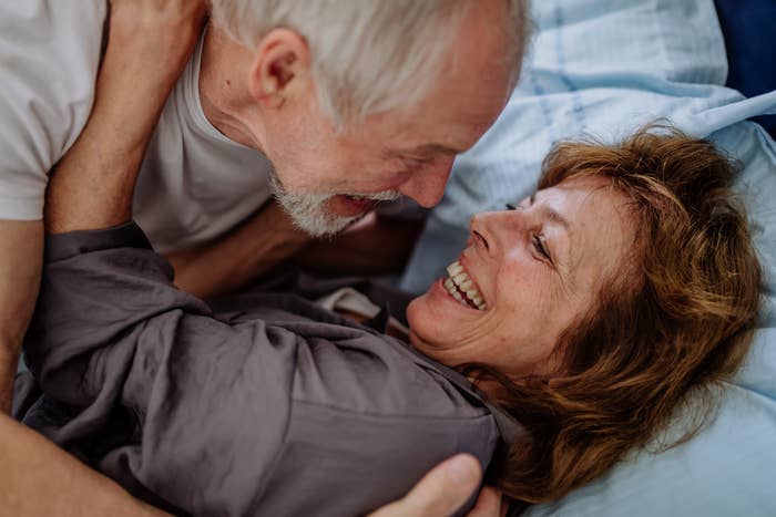 Older couple laughing and embracing in bed, sharing an intimate and joyful moment