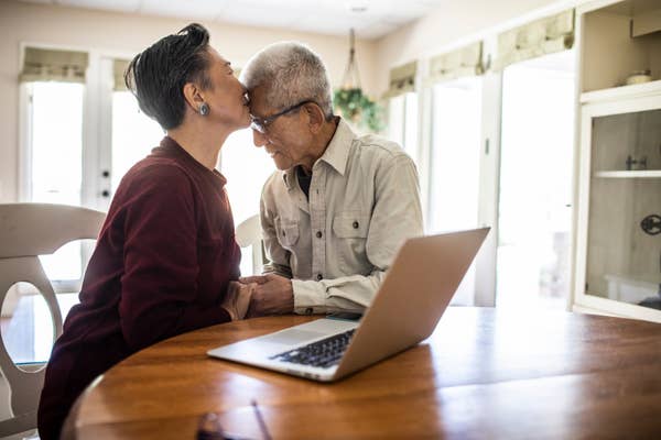 Elderly couple sharing a tender moment at a table with a laptop, symbolizing love and connection